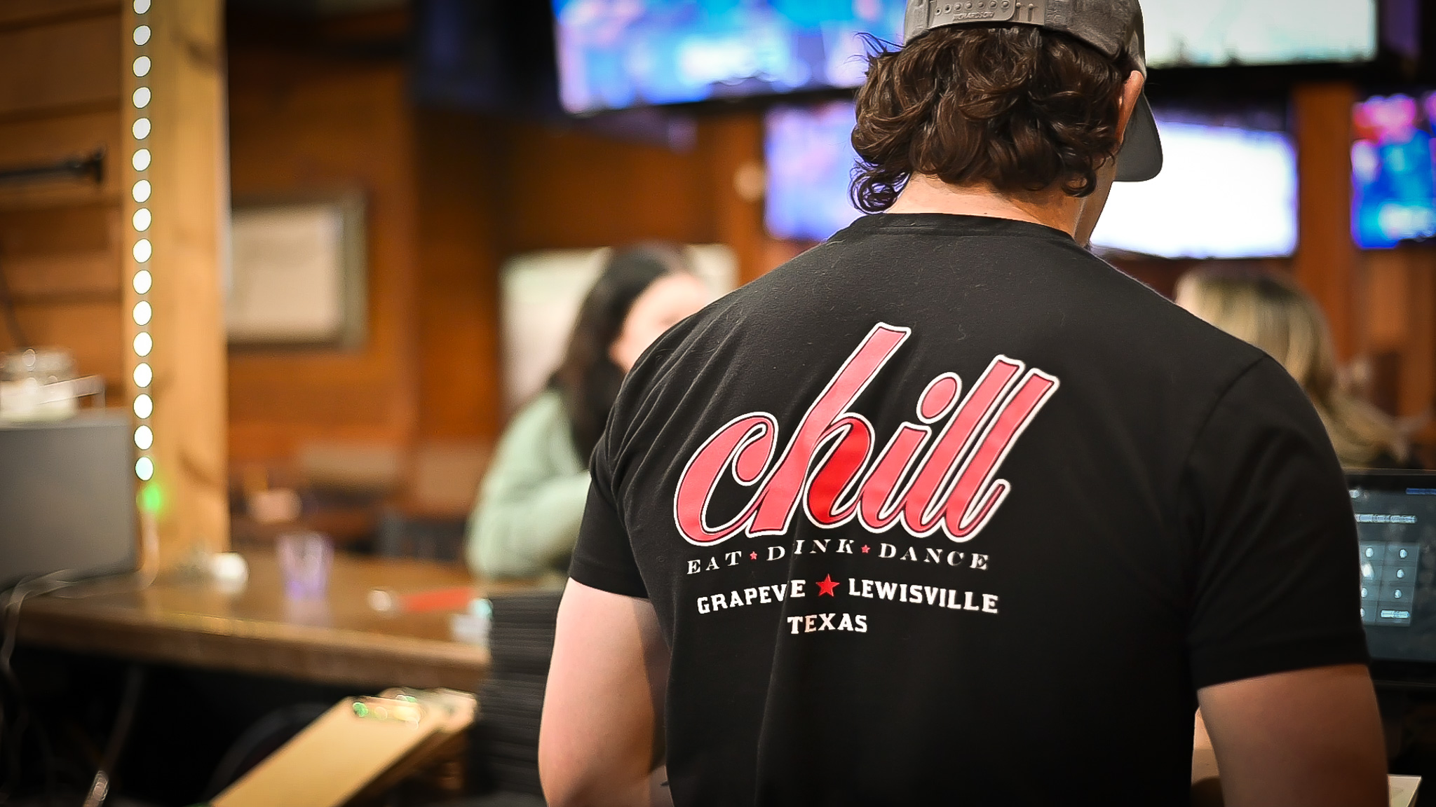 Inside Chill Bar & Grill Lewisville — sports bar staff wearing the branded Eat · Drink · Dance T-shirt