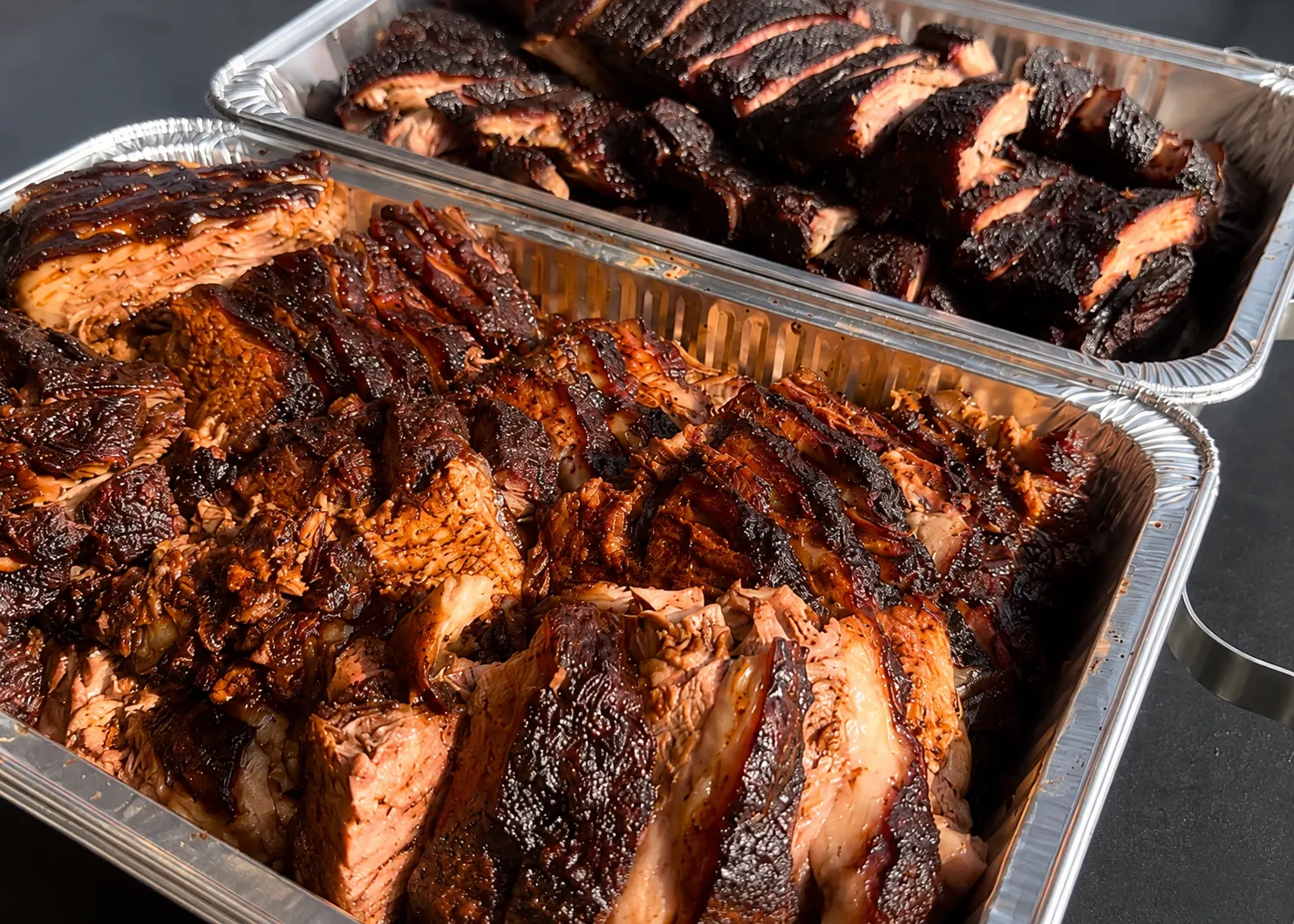 Two foil catering trays packed with sliced smoked brisket