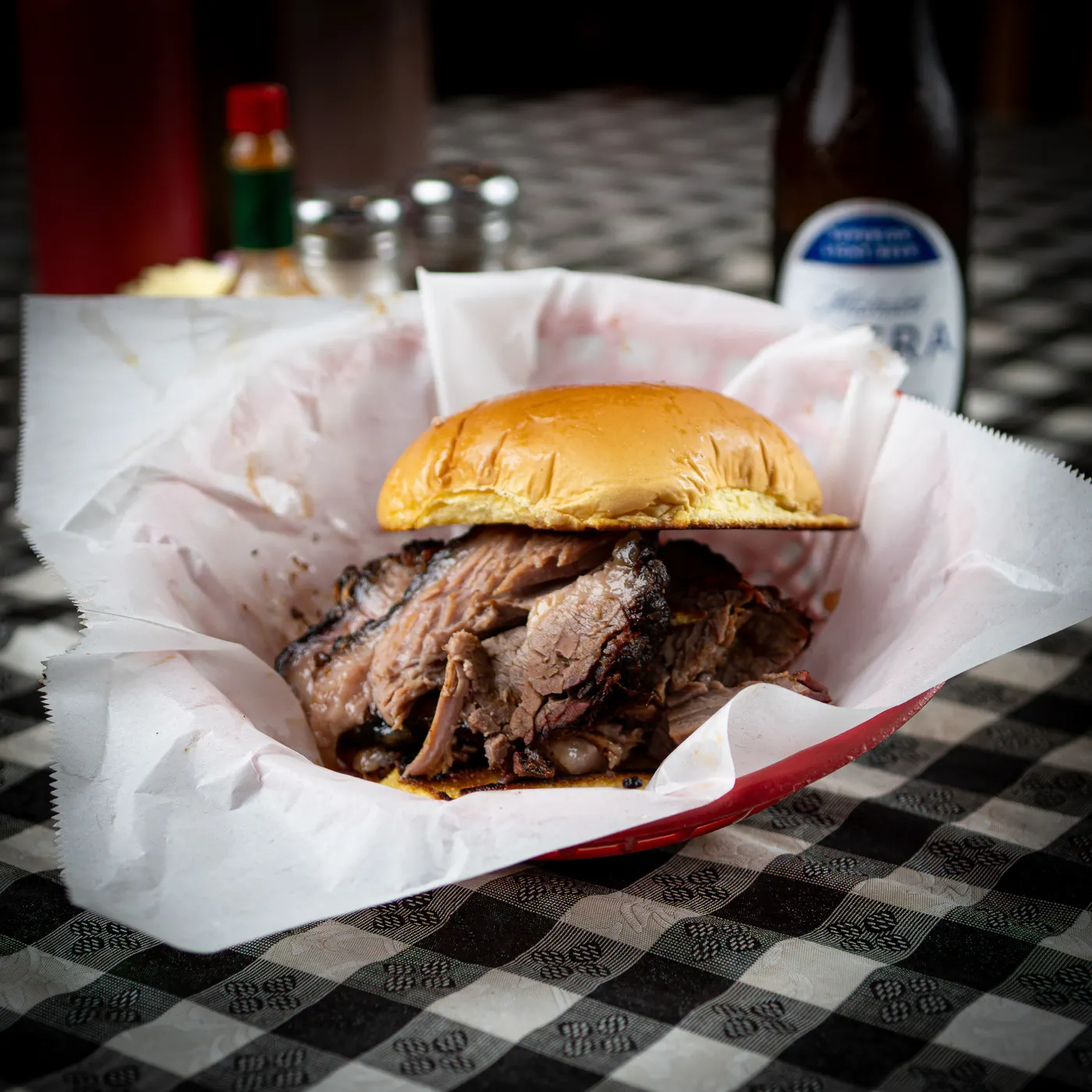 A chopped brisket sandwich on a bun in a paper-lined red basket