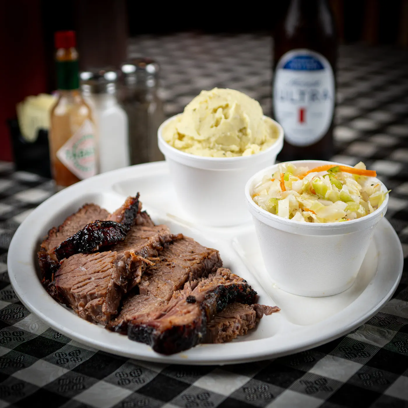 Sliced smoked brisket on a plate with potato salad and coleslaw