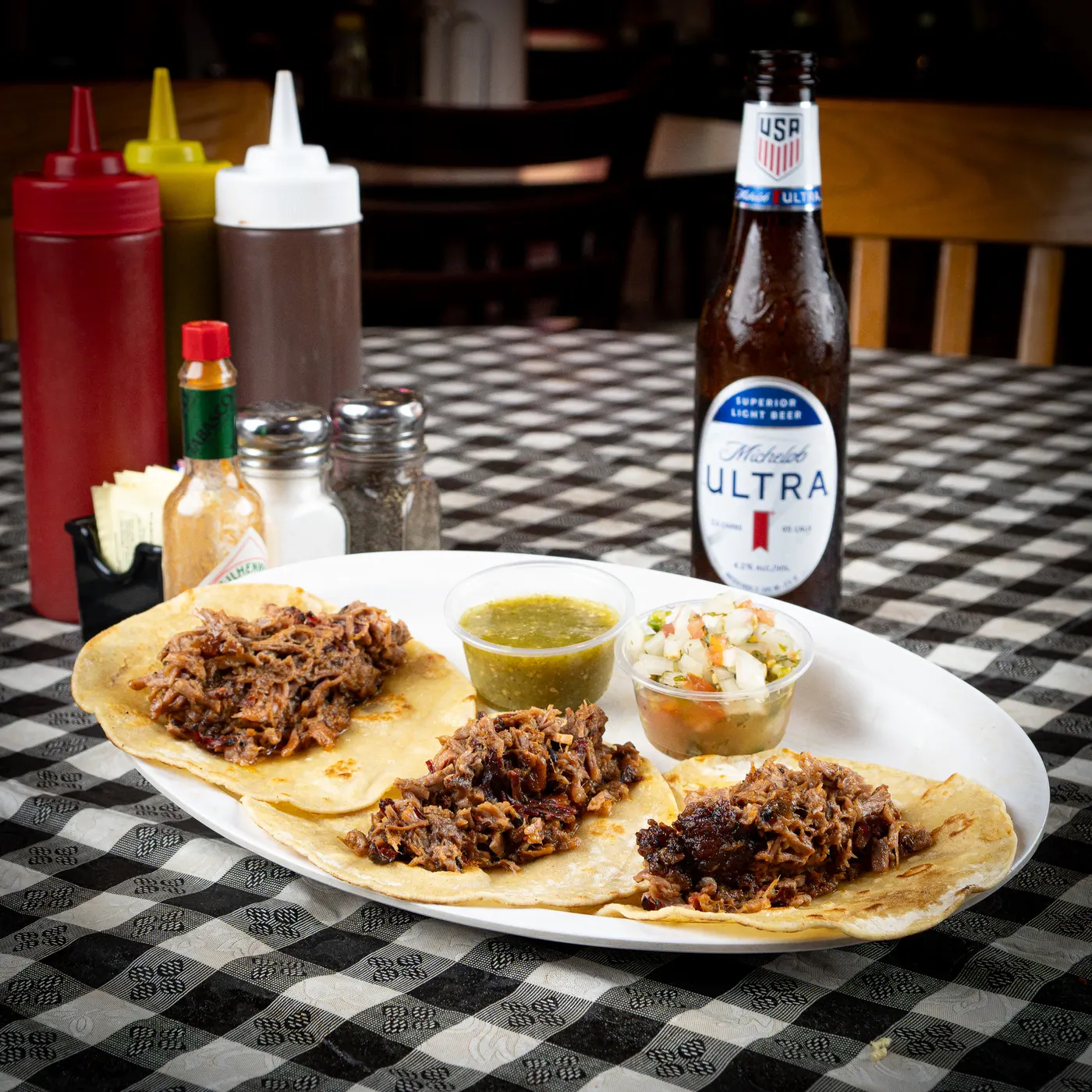 Three chopped brisket tacos on a plate with salsa and slaw