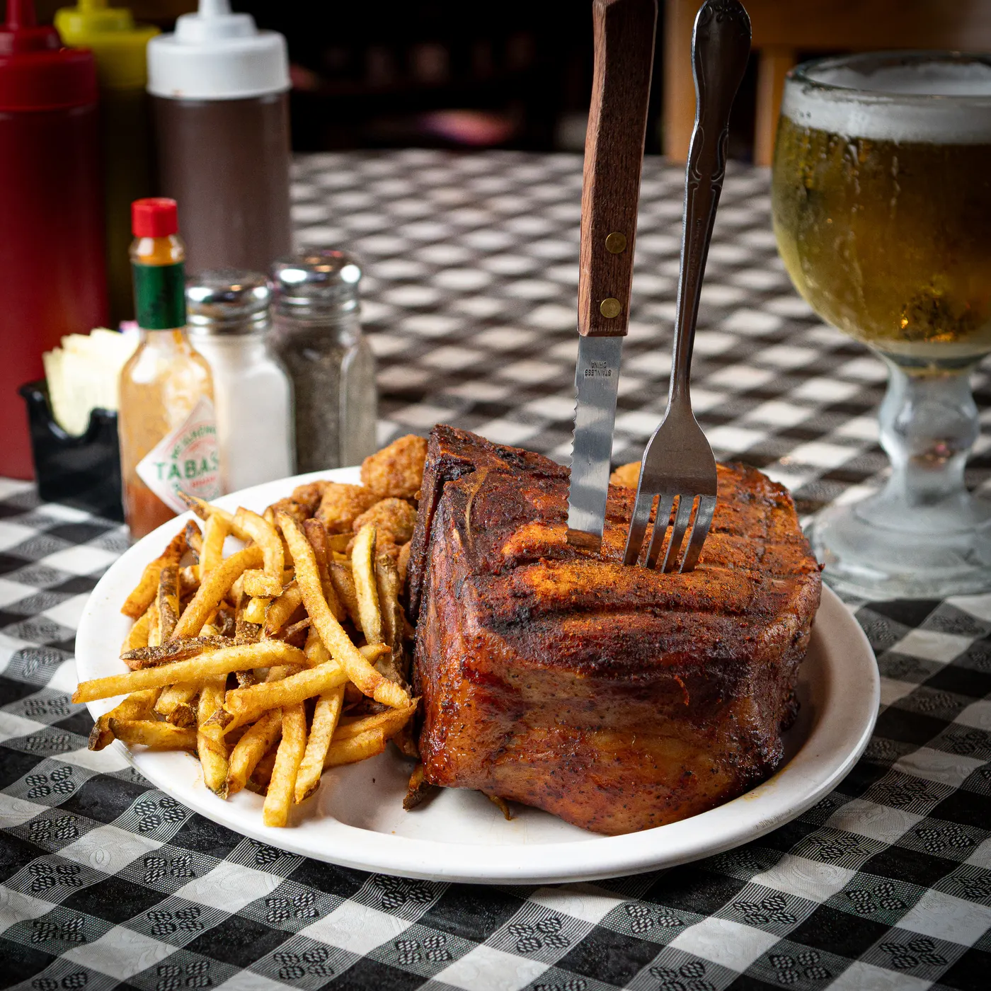 A thick smoked pork chop with hand-cut fries, a fork standing in the meat
