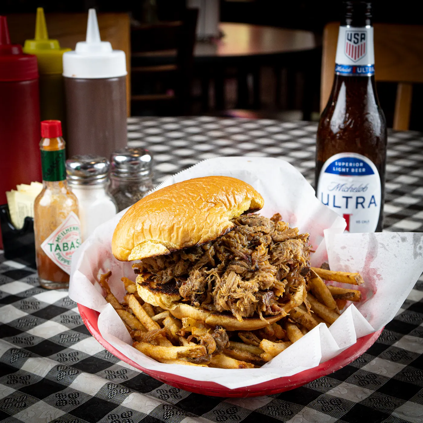 A pulled pork sandwich piled high in a basket with hand-cut fries