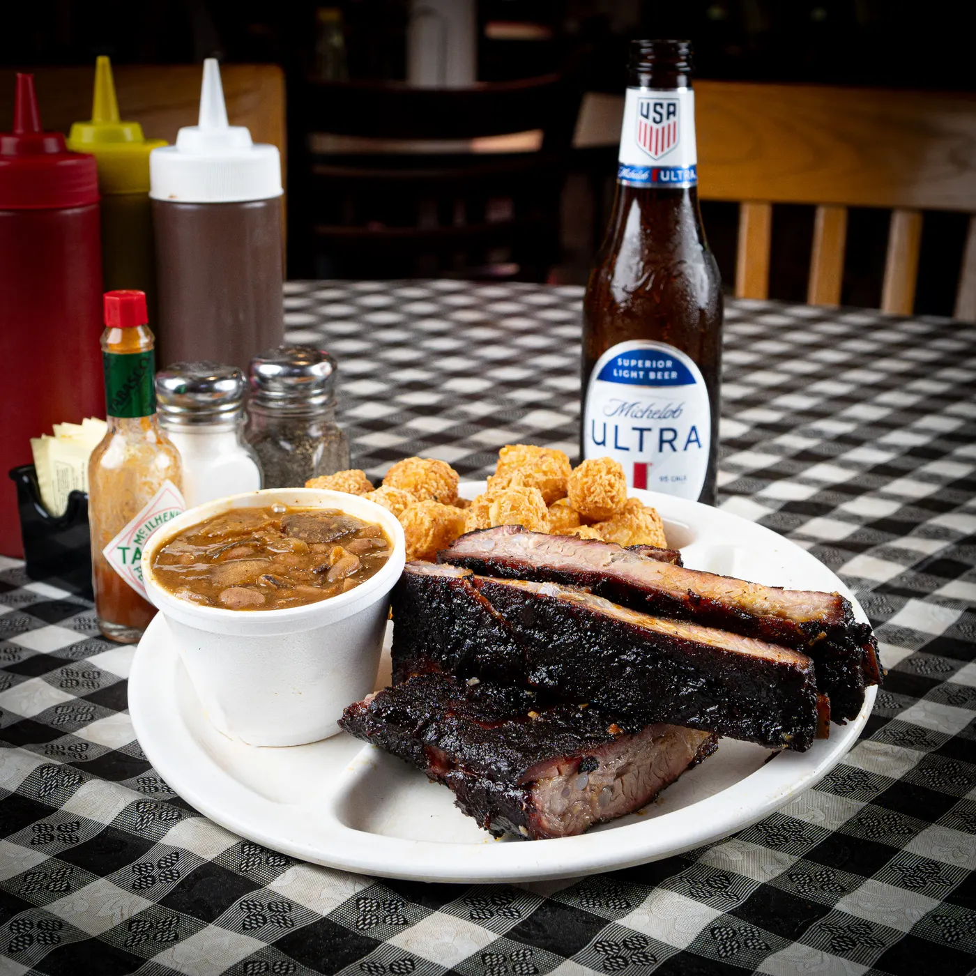 Smoked pork ribs on a plate with tater tots and a cup of beans