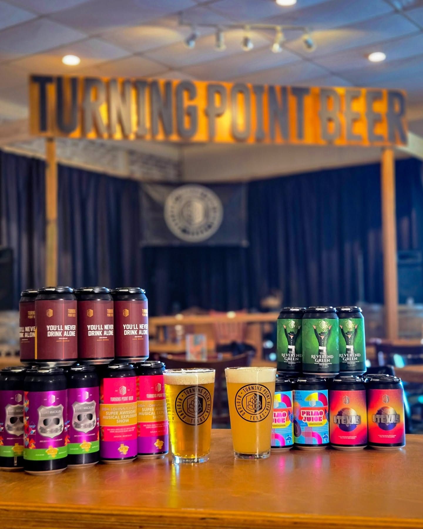 Stacked four-packs and fresh pours lined up on the bar under the Turning Point Beer sign