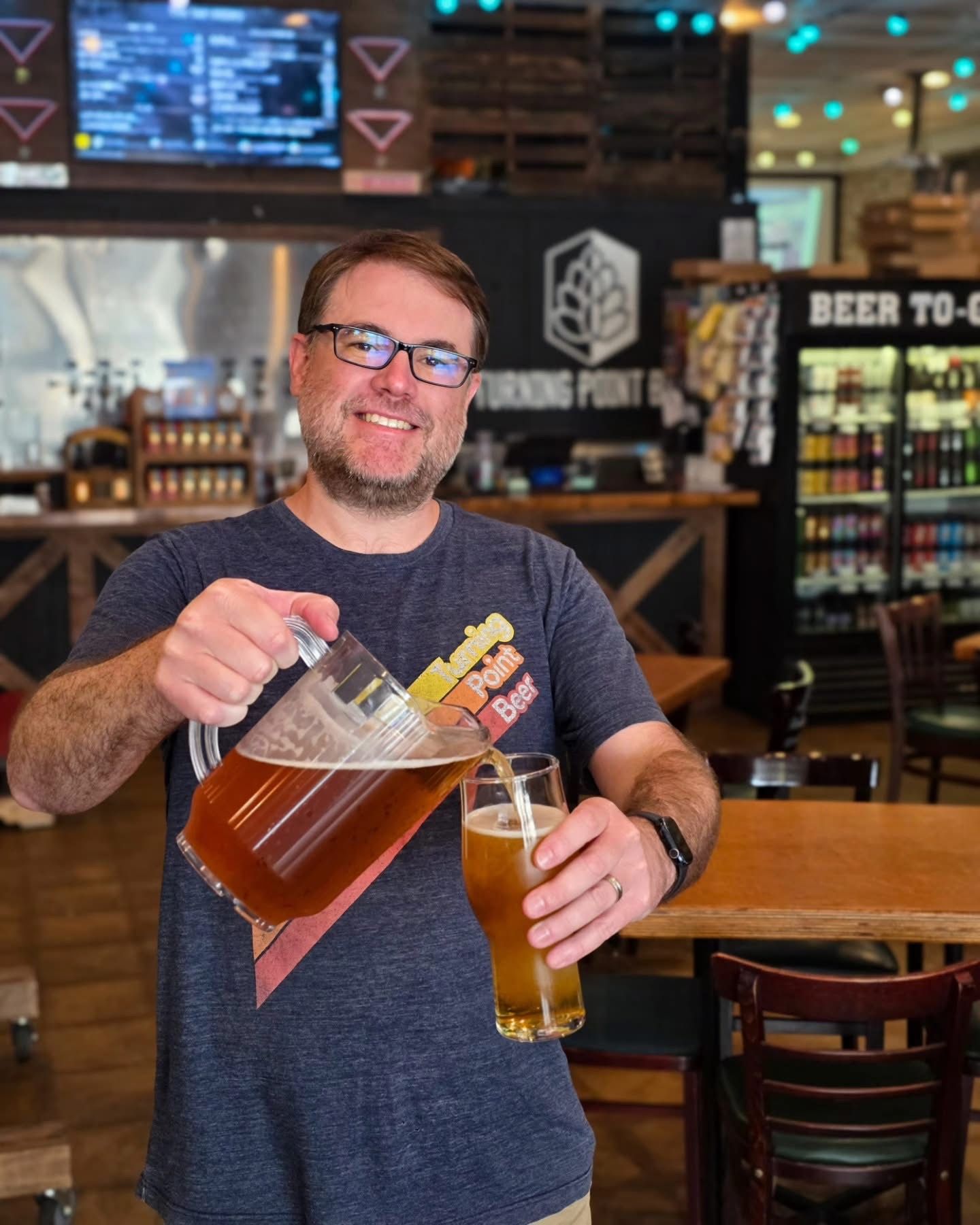 A staff member pouring a pitcher at the bar in front of the beer to-go fridge