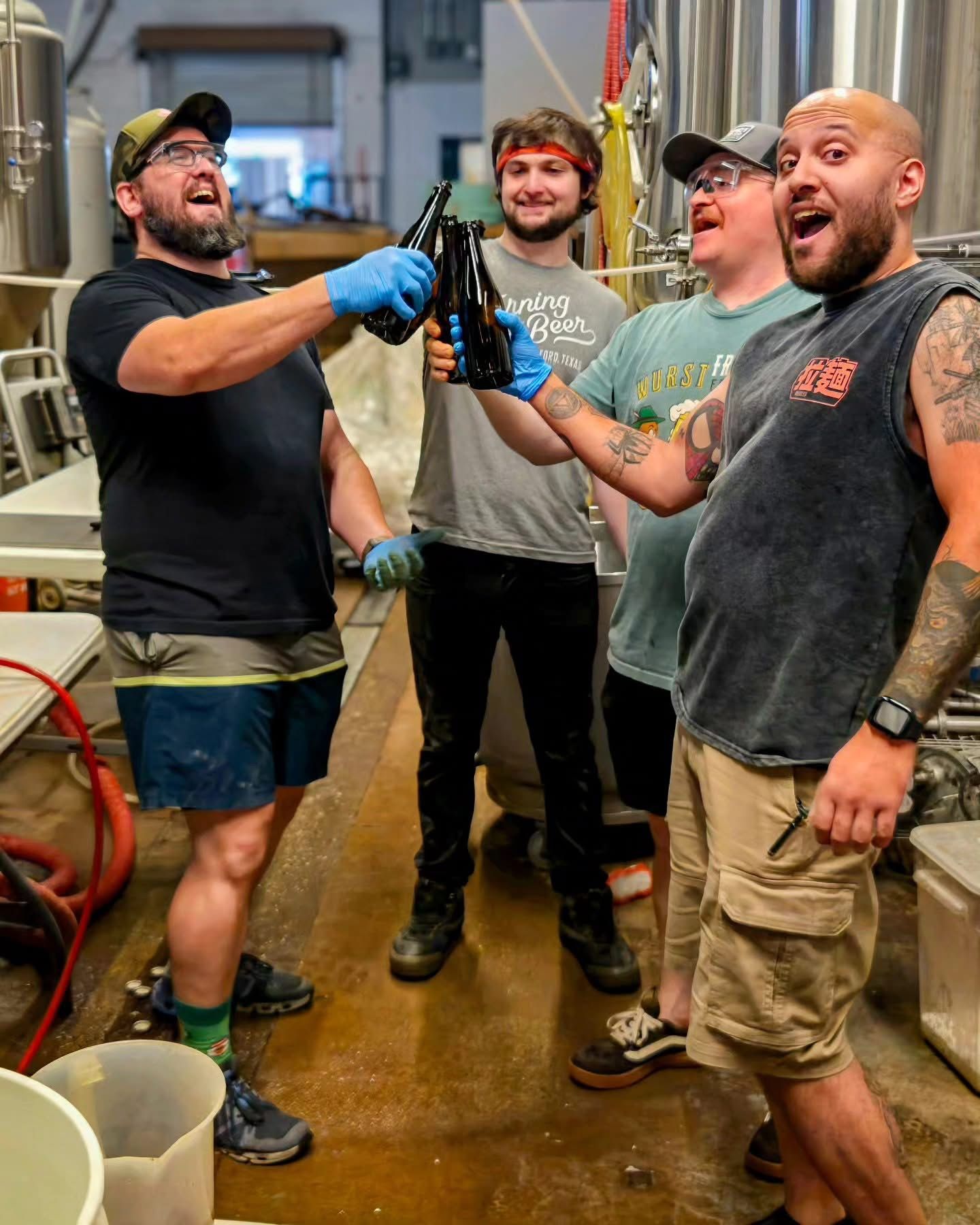 Four of the crew cheering with bottles raised in the brewhouse