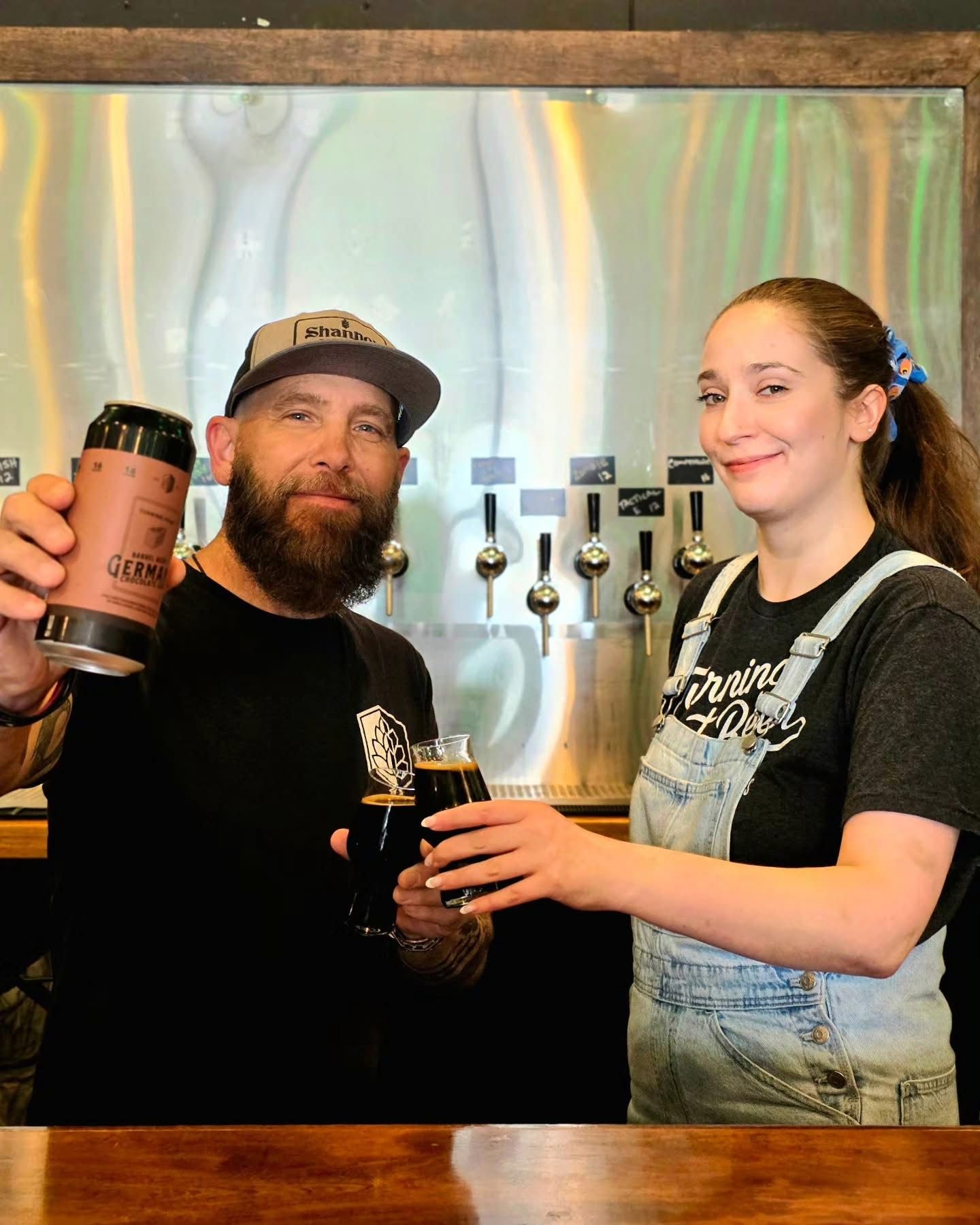 Two staff members toasting a stout in front of the tap wall