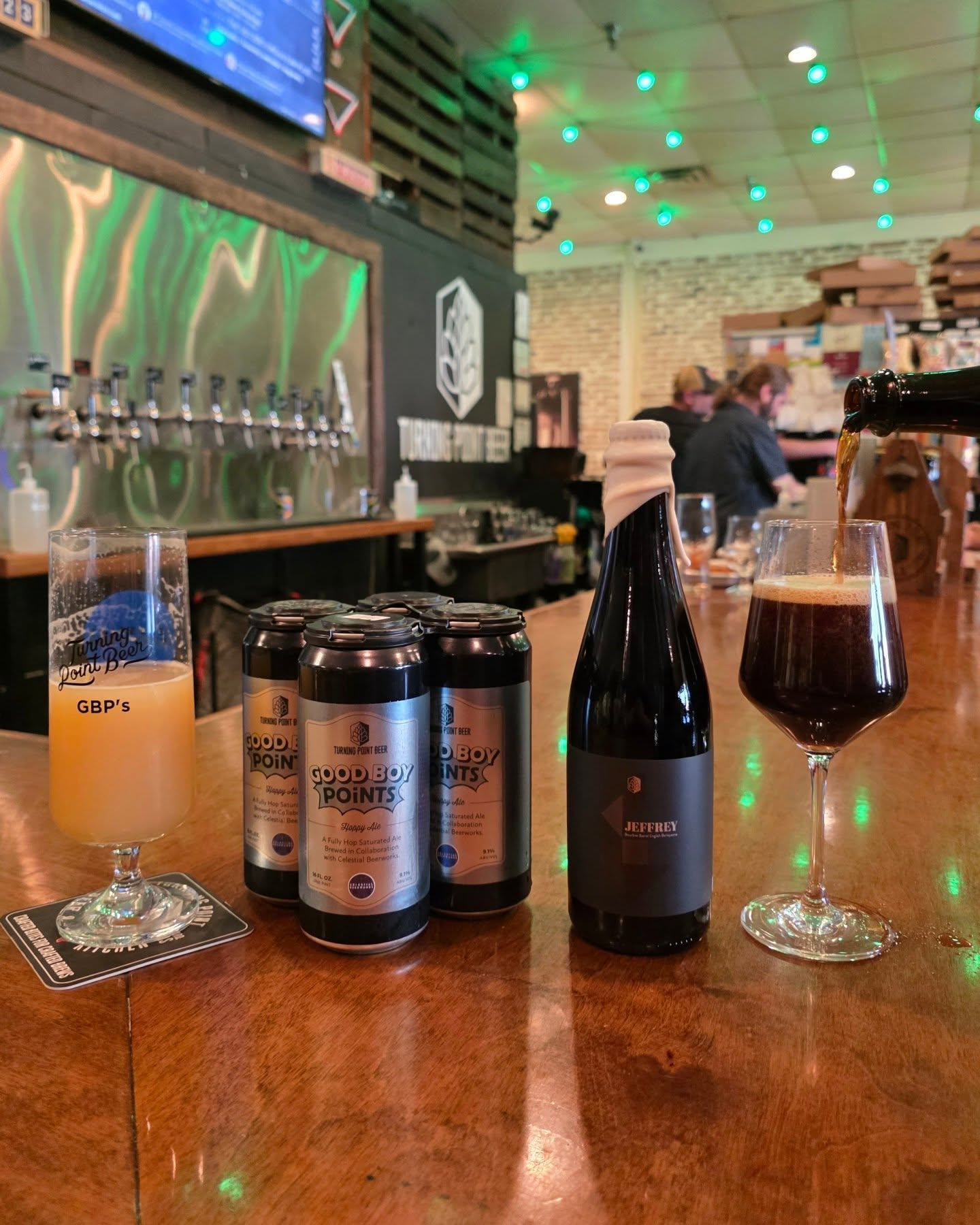 The bar and tap wall under the Turning Point hop mark, with a four-pack, a bottle, and a dark pour on the counter